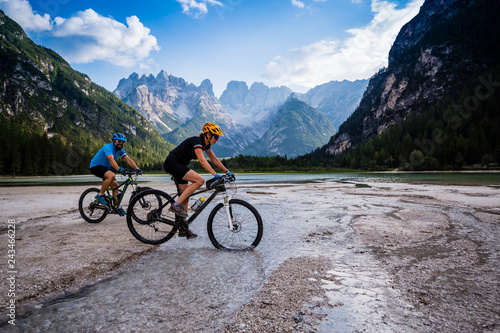 Tourist cycling in Cortina d'Ampezzo, stunning rocky mountains on the background. Family riding MTB enduro flow trail. South Tyrol province of Italy, Dolomites. photo