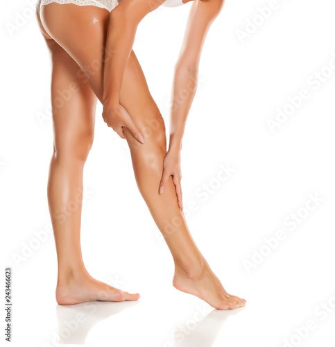 Young woman applying cream on her legs on white background