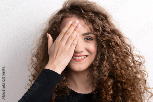 Young beautiful happy woman in studio, covering her eye.