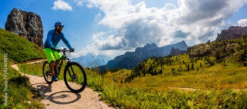 Tourist cycling in Cortina d'Ampezzo, stunning Cinque Torri and Tofana in background. Man riding MTB enduro flow trail. South Tyrol province of Italy, Dolomites. © Gorilla