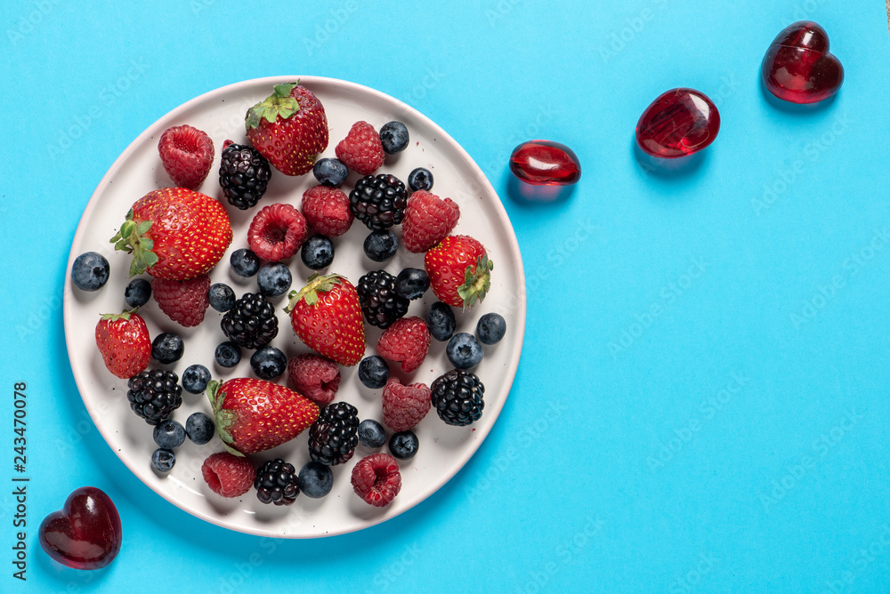 Top view plate with variety of forest fruits, berries and hearts on a blue background Top view plate with variety of forest fruits, berries and hearts on a blue background