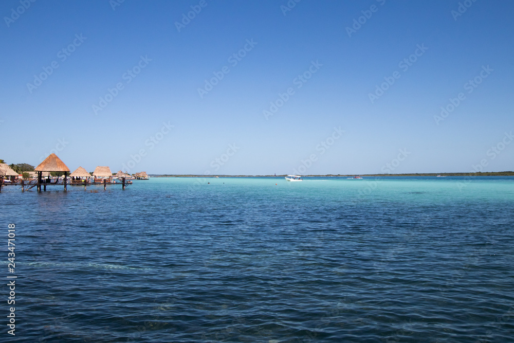 blue and blue Caribbean sea with crystal clear waters and clear sky. a bungalow with a pier in the middle of the lagoon in a coral reef. hotel and rooms by the sea