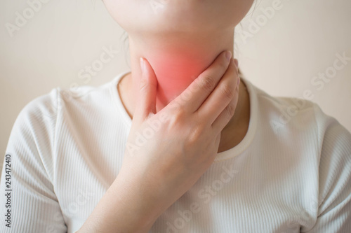 Sick women suffering from sore throat on gray background. Causes of throat pain include flu, common cold, bacterial infections, allergies, smoke, GERD or tumor. Health and medical concept. Close up. photo