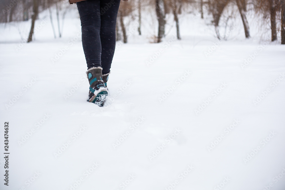 The girl walks in the snow in dark jeans and gray boots with blue soles and blue stripes The girl walks in the snow in dark jeans and gray boots with blue soles and blue stripes