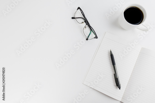 Top view on a freelancer/ blogger/ writer workspace. White table top with black headphones, pen, cup of coffee and empty notebook. Flat lay with copy space.