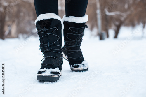 Black winter women's boots with white fur and white soles on the snow in the park