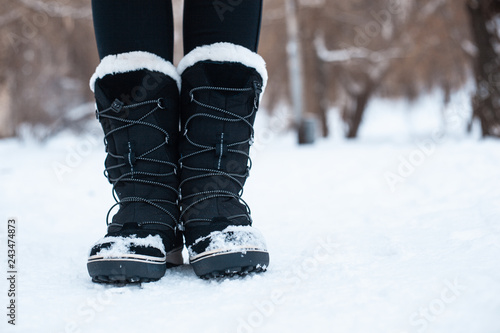 Black winter women's boots with white fur and white soles on the snow in the park