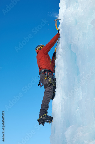 Alpinist man with ice tools axe climbing a large wall of ice. Outdoor Sports Portrait.