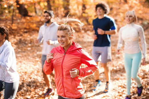Small group of people running in woods in the autumn. Selective focus on blonde woman.
