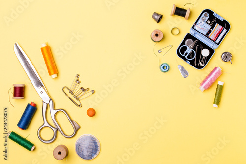 Composition with threads and sewing accessories - scissors, centimeter, pins on yellow background.