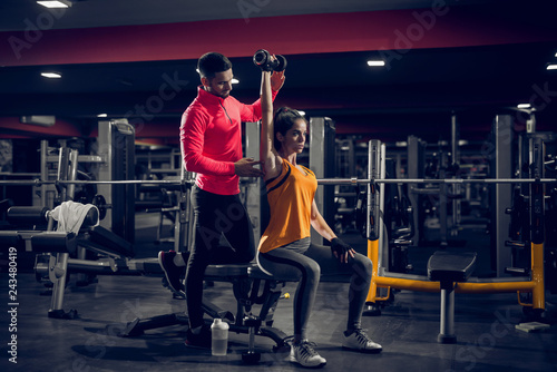 Picture of personal trainer helping her client to lift weight in a gym.