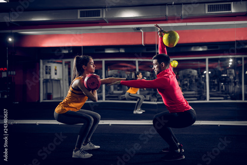 Couple goals. Fit young couple working out in a gym . Doing squats while holding weights in their hands.
