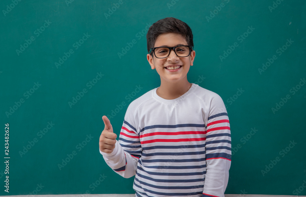 Portrait Of Boy Gesturing Thumbs Up Sign Against Blackboard	