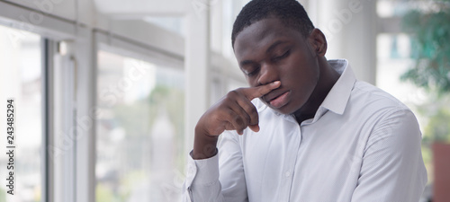 Sick African man with runny nose; Portrait of ill black man suffering from runny nose due to cold; flu; allergy; polluted air; dust; smog; air pollution sickness concept; African young adult man model photo