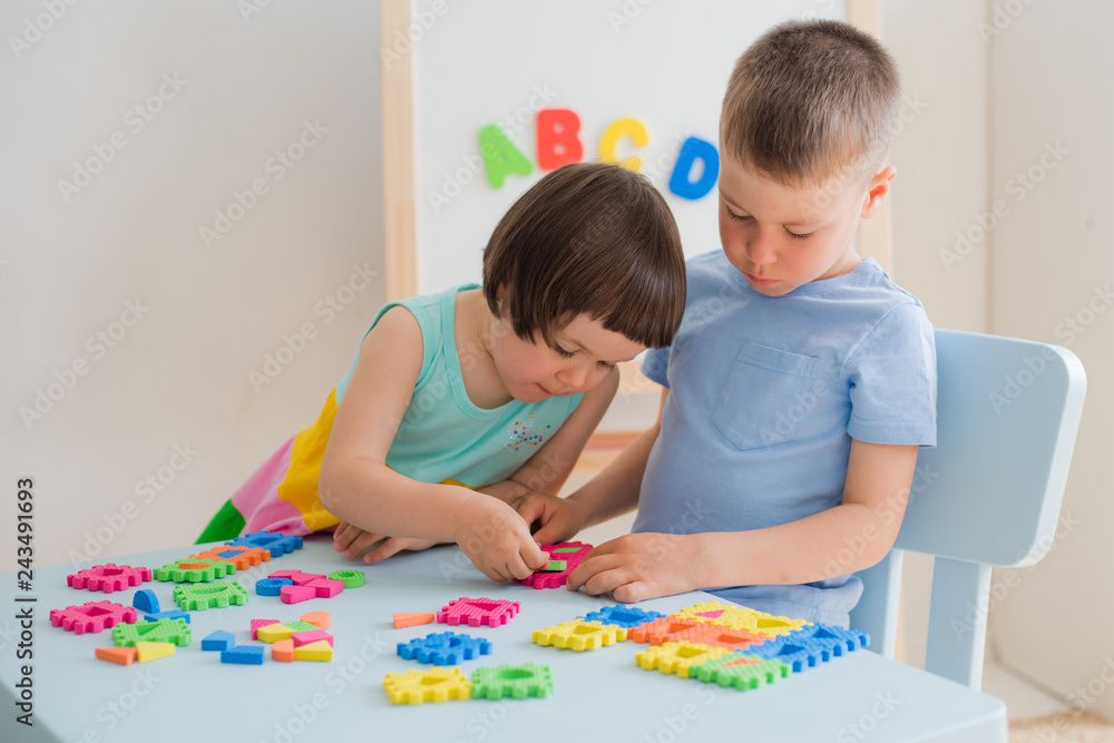 Fototapeta premium A boy and a girl collect a soft puzzle at the table. Brother and sister have fun playing together in the room.