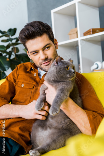 happy man with british shorthair cat sitting on sofa at home