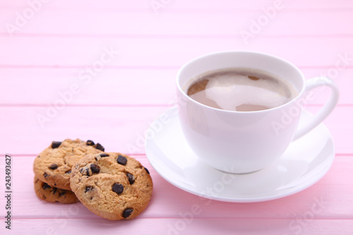 Cup of coffee with chocolate cookies on pink background