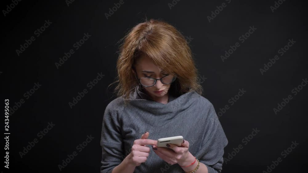 Closeup portarit of modern middle-aged woman scrolling on her phone casually with the background isolated on black Closeup portarit of modern middle-aged woman scrolling on her phone casually with the background isolated on black