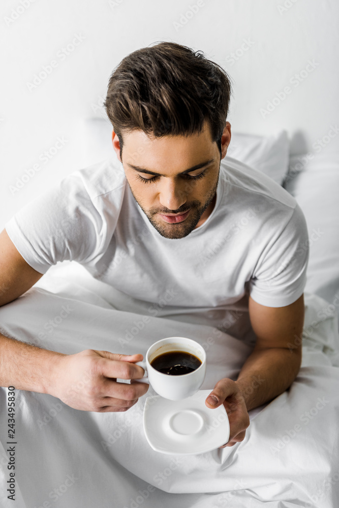 handsome smiling man in pajamas holding cup of coffee in bed handsome smiling man in pajamas holding cup of coffee in bed