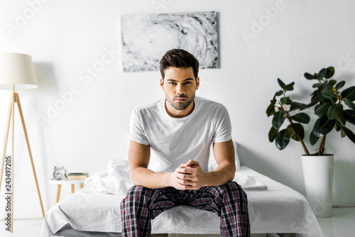 handsome confident man in pajamas sitting on bed at home