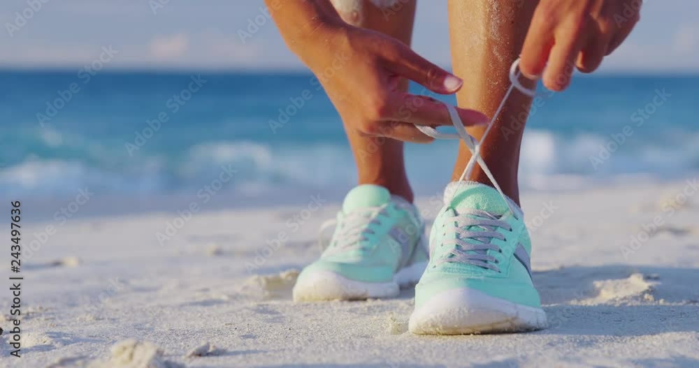 Runner woman tying laces of running shoes preparing for beach jogging. Closeup of hands lacing cross training sneakers trainers for cardio workout. Female athlete living a fit and active life.