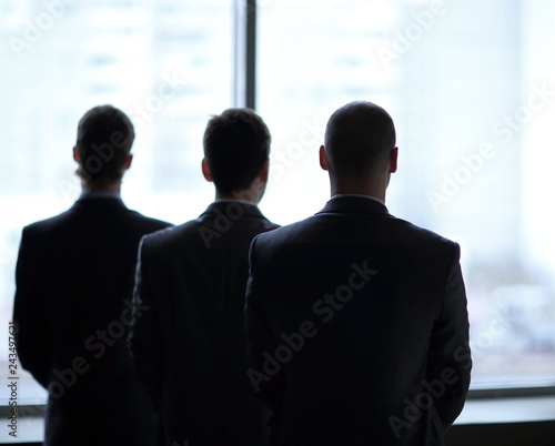 rear view of three businessmen as they stare at the big window overlooking the city