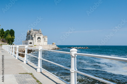 Fototapeta Naklejka Na Ścianę i Meble -  Black sea quay in Constanta, Romania with  the cast iron white painted railing along the water front and the now abandoned baroque architectural gem old casino building in the backdrop.