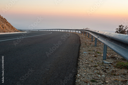 Highway high in the mountains with a mixed cross profile and a heavy guardrail mounted on the road shoulder.