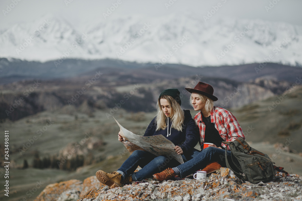 Female traveler hipsters sit and view map amid beautiful mountains