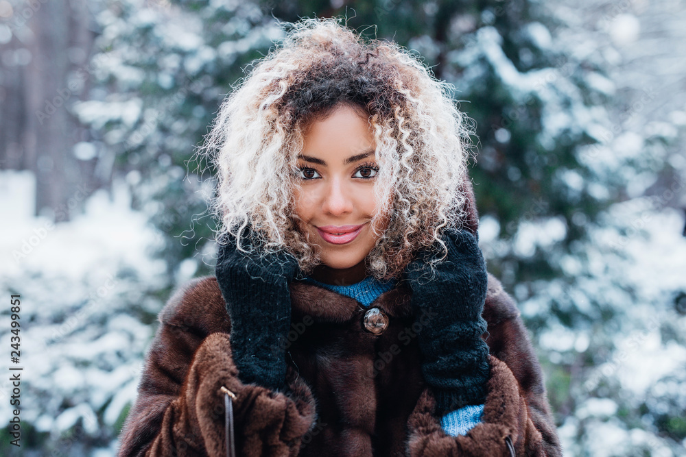 Fototapeta premium Close-up portrait of beautiful young afro american woman in snow winter forest