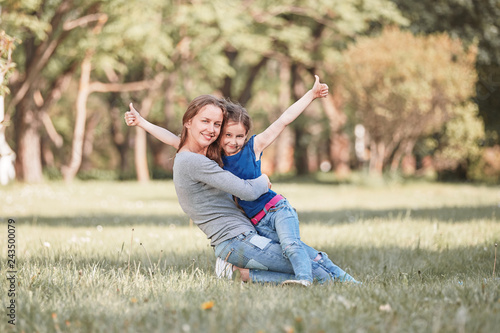 happy mom hugging her little daughter sitting on the lawn summer day © yurolaitsalbert