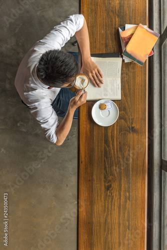 High angle view of young man enjoy free day, reading book, drinking coffee