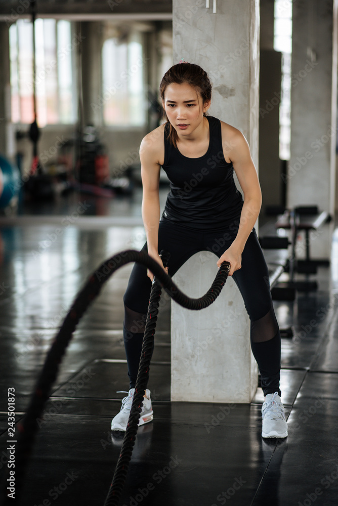 Athletic asian woman exercising with battle rope at gym