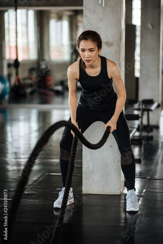 Athletic asian woman exercising with battle rope at gym