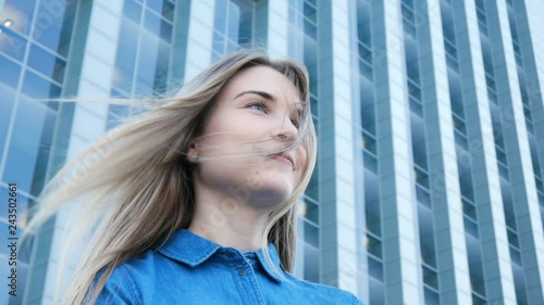 Low-angle portrait of a pretty girl with beautiful blue eyes and long hair with modern architecture on the background