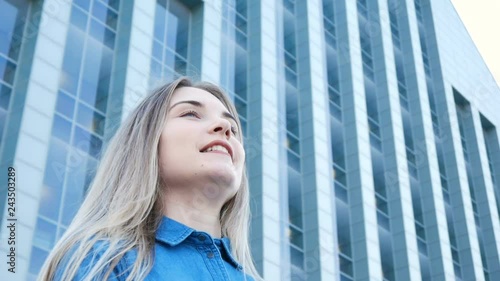 Low-angle portrait of a pretty girl with beautiful blue eyes and long hair with modern architecture on the background