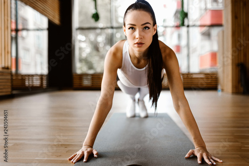 Beautiful slim dark-haired girl dressed white sports clothes is doing is doing plank in the gym