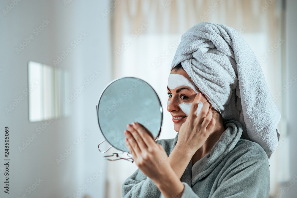 Smiling young woman holding a mirror and applying face cream. Smiling young woman holding a mirror and applying face cream.