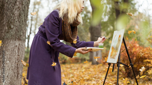 Blonde girl artist draws among falling leaves in the autumn park photo