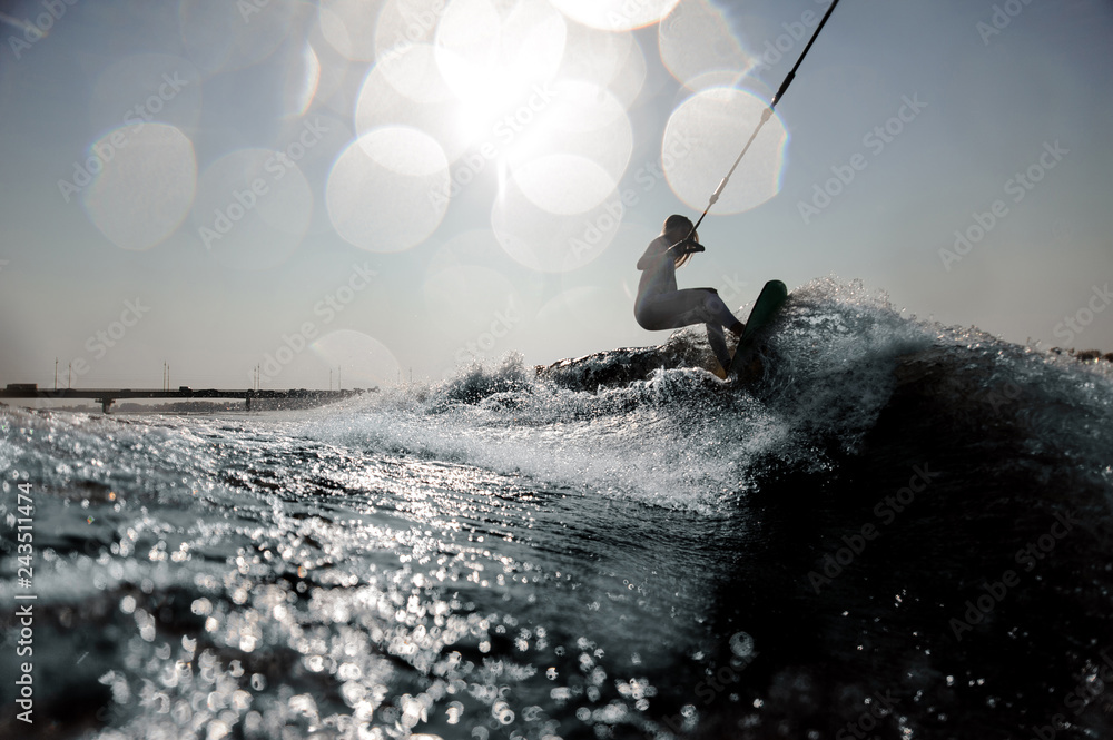 Blonde girl riding on the wakeboard holding a rope