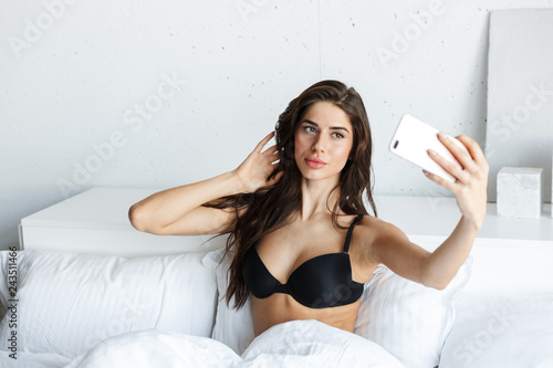 Premium Photo  Photo of a beautiful confused displeased brunette woman  wearing lingerie using mobile phone lies in bed.