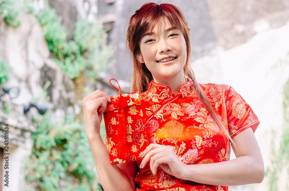 Portrait charming beautiful asian woman wear cheongsam dress gets red envelopes from her family. Pretty girl shows red envelopes. Gorgeous girl feel happiness and she has nice smile.