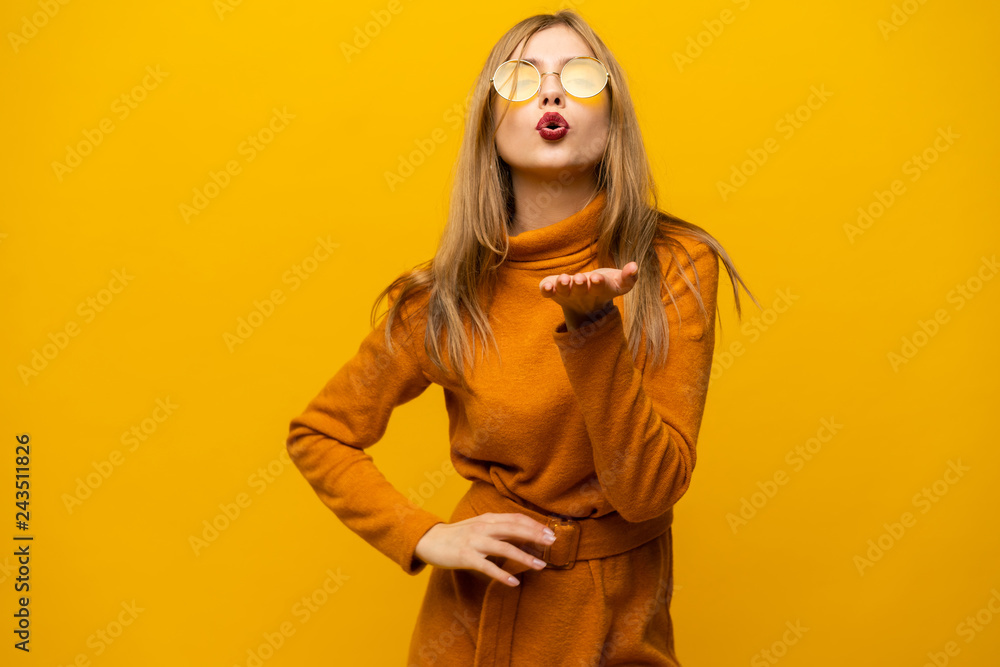 Excited young woman in orange dress, widely smiling, looking at camera. Isolated on yellow background