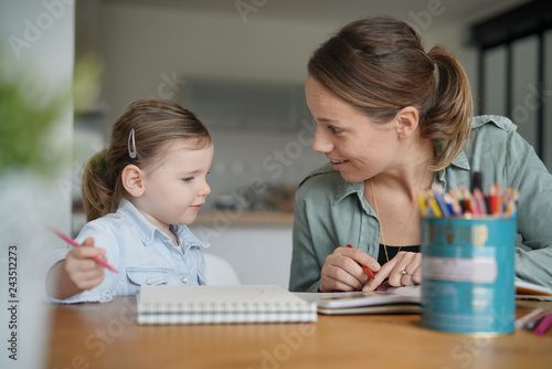 Mother and young daughter drawing and reading together at home