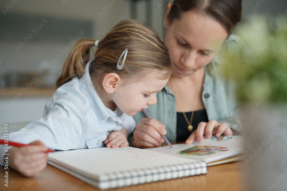 Mother and young daughter drawing and reading together at home Mother and young daughter drawing and reading together at home