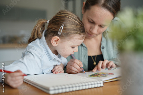 Mother and young daughter drawing and reading together at home