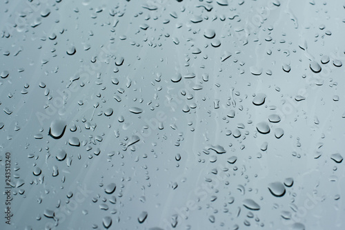 Rain drops on a window glass surface against a dark background of stormy sky.