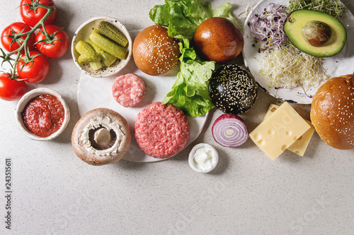 Ingredients for cooking homemade traditional and vegan hamburgers. Meat beef burger, cheese, avocado, portobello, tomato, black and white buns, salad, cucumbers. Grey background. Top view, space.