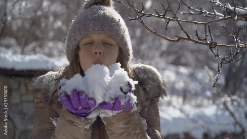 Beautiful girl on a Sunny winter day blowing in the snow. Young teen girl blowing on snow in camera. Slow motion video