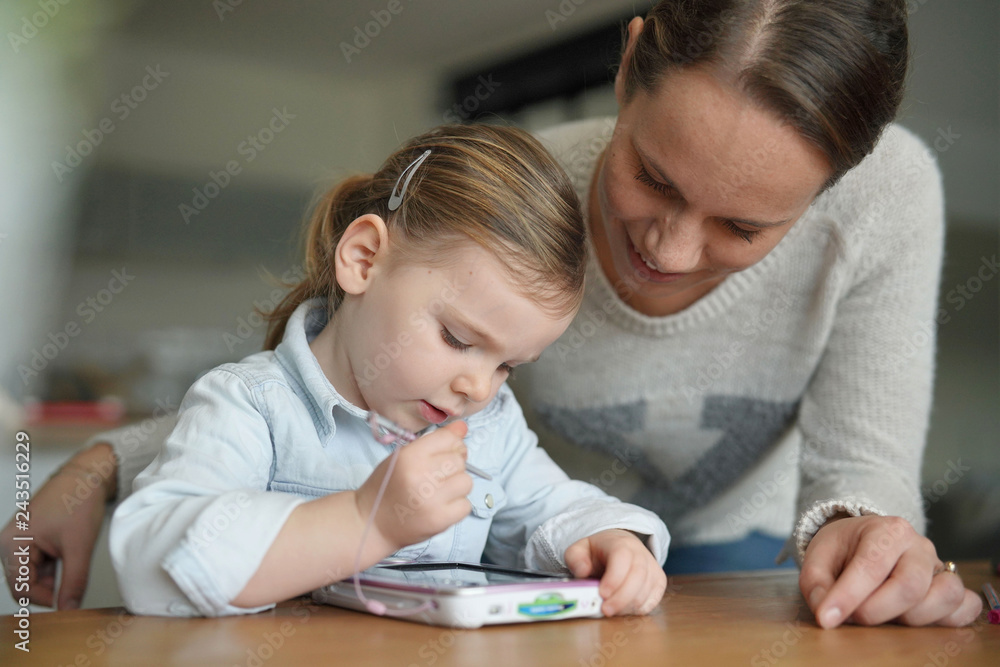 Mother and daughter having fun playing with child's tablet at home Mother and daughter having fun playing with child's tablet at home